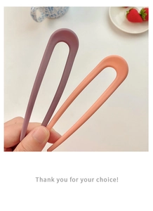 Detail of hand holding matte purple and orange U-shaped hairpins in a minimalist style