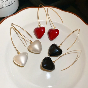 Close-up of three pearl heart pendant earrings in red, white and black on a ceramic plate