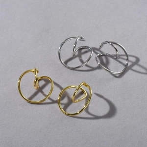 Detailed view of geometric gold and silver spiral ear clips on grey background