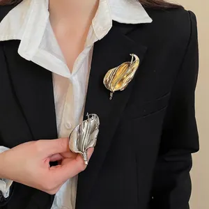 Artistic metal leaf brooches in gold and silver finish on a formal black blazer
