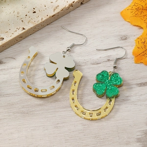Close-up of golden horseshoe earrings with green glitter clover on wooden background