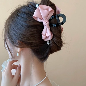 Detail view of a pink satin bow hair claw clip with rhinestone tassels on a model