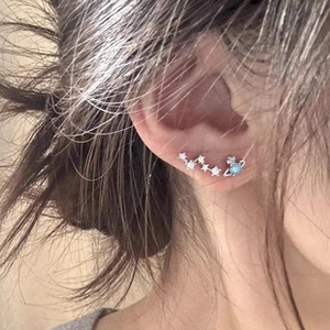Close-up of star-shaped zircon studs and blue Saturn planet earrings on model's ear