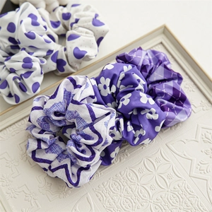 Flat lay of three purple patterned elastic hair scrunchies on a textured white plate