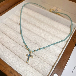 Detailed shot of light blue beaded choker necklace with gold cross pendant and blue zircon