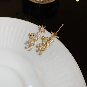 Detailed close-up of golden bear and star earrings with pavé rhinestones on white plate