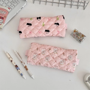 Flat lay of pink quilted pencil cases with cute cat and rabbit patterns on a white desk