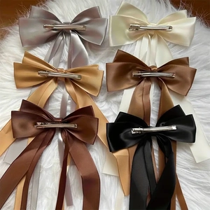 Set of 6 satin ribbon bow hair clips in various colors laid on a soft white texture