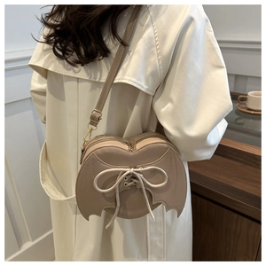Detail of beige heart-shaped bag with bat wings and lace-up ribbon on a model