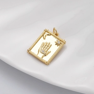 Macro shot of gold Hamsa hand charm with moon and stars on a white ceramic plate