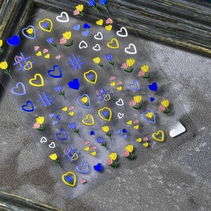 Detail of 3D embossed nail stickers featuring blue and yellow doodle flowers on a grey base