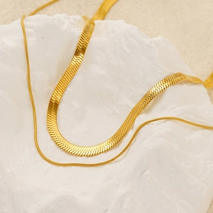 Double-layered golden snake chain and flat link necklace on white marble base