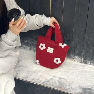 Detail of red plush tote bag featuring floral embroidery and white logo patch