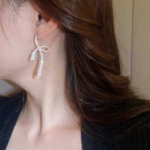 Close-up of sparkling silver bow earrings with micro-pave zircons on model ear
