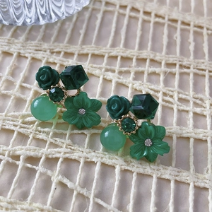 Detail view of green rose and crystal flower earrings on white woven fabric texture