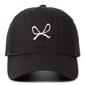 Close-up of white bow embroidery on a black cotton baseball cap with ventilation eyelets