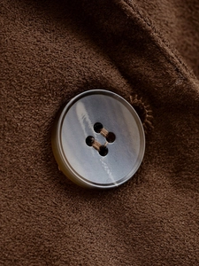 Gros plan sur la texture veloutée de la veste olive et son bouton aspect marbre