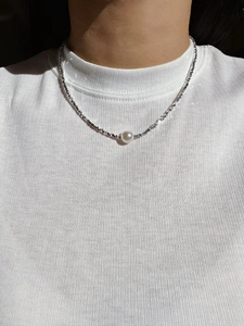 Close-up of a round white pearl pendant on a shiny silver necklace worn by a model