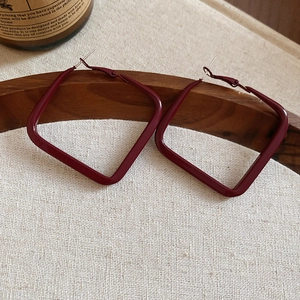 Macro detail of wine red square hoop earrings with silver pins on a vintage wooden tray