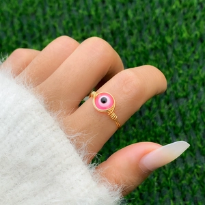 Macro shot of handmade gold wire-wrapped ring with pink evil eye bead detail