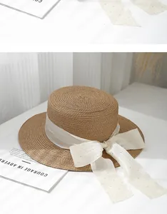 Detail of flat top straw hat with wide white gauze ribbon and large bow decoration