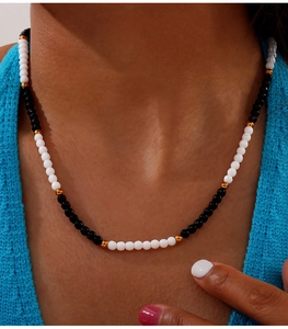 Detail of beaded necklace with white and black stones worn against a blue sweater