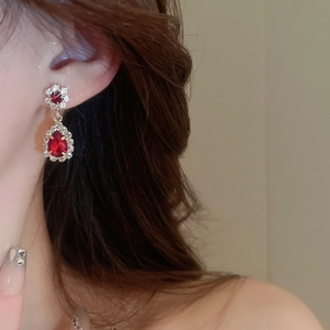 Close-up of elegant gold earrings with red gems and sparkling diamonds on a female model