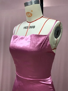 Détail macro de la robe en satin fuchsia brillant avec fines bretelles et texture soyeuse