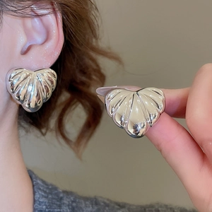 Macro detail of silver heart earrings with shell-style ribbed texture on a model