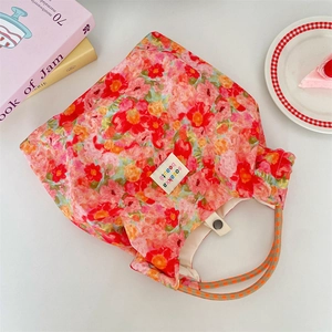 Close-up of floral tote bag with metal snap closure and brand label on white surface