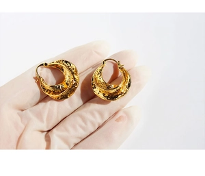 Macro detail of gold earrings with irregular hammered texture on a gloved hand