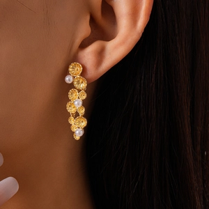 Detailed close-up of gold flower-shaped metal disks and dangling pearl tassel earrings