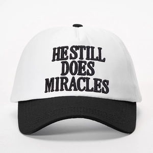 Detailed close-up of HE STILL DOES MIRACLES embroidery on two-tone baseball cap