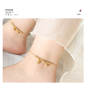 Detail of a golden beaded anklet with bell charms on a model's ankle with a soft background