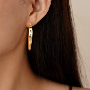Close-up of model wearing gold polished hoop earrings with minimalist engraved lettering