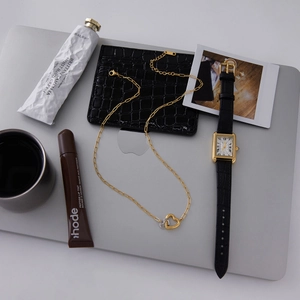 Flat lay of interlocking heart necklace and gold watch with minimalist accessories