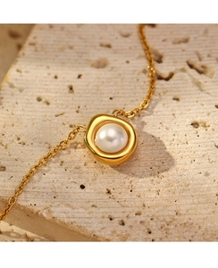 Macro detail of gold pearl pendant necklace on natural stone with irregular gold frame