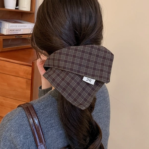 Detail of dark plaid fabric bow hair tie worn on low ponytail in a cozy indoor setting