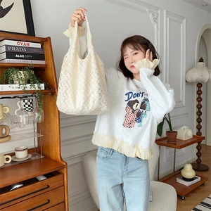 Close-up of beige mesh floral tote bag detail worn by a model in a cozy interior setting