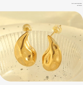 Macro shot of gold teardrop earrings with fluid ripple texture on glass edge