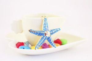 Detailed view of blue starfish keychain charm with gold edges on white ceramic cup