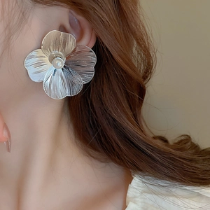 Detail of silver flower stud earring with central pearl on model, elegant metallic texture