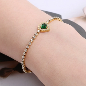 Detailed view of a gold tennis bracelet featuring a green heart-shaped emerald stone