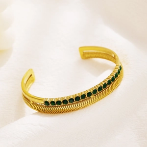 Detail of golden double-layer herringbone bracelet with green gemstones on white fabric