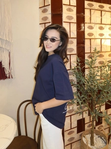 Detail view of a loose navy blue t-shirt with print, styled with white trousers and sunglasses