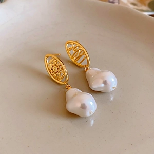 Detail view of gold-plated hollow earrings with baroque pearls on a beige ceramic tray