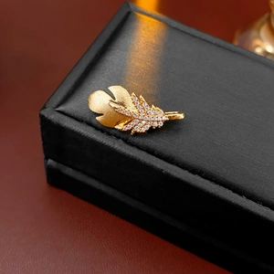 Macro shot of gold feather brooch with white zircon inlay on textured black jewelry box