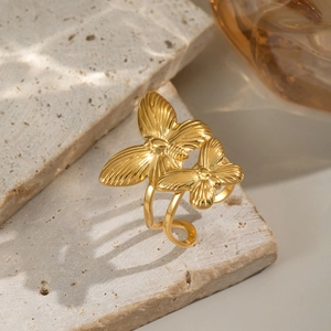 Macro detail of gold 18K butterfly open ring with textured wings on beige stone pedestal
