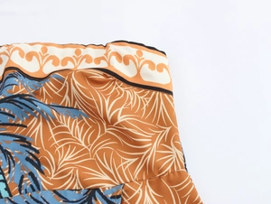 Detail of tropical palm tree print on orange strapless dress with smooth fabric texture