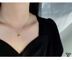 Macro close-up of a polished gold heart pendant on a thin chain worn by a model